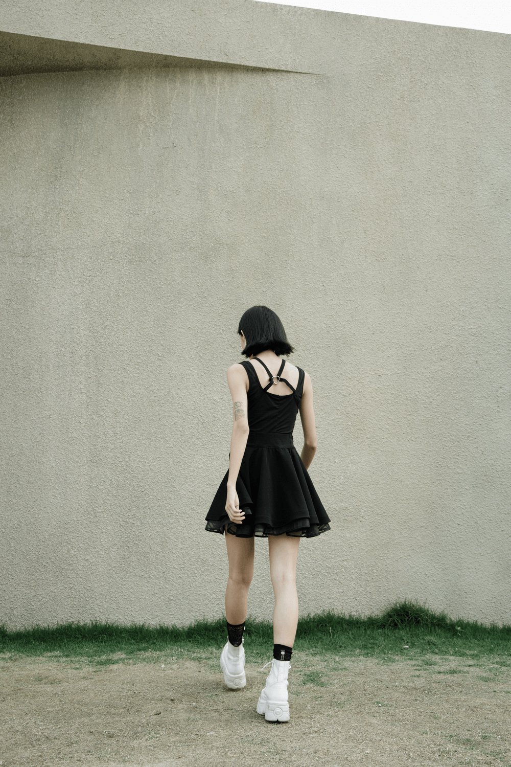 Back view of a person wearing a punk style high waist layered skirt walking on a grassy area.