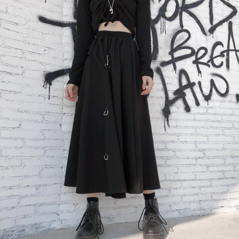 Punk style irregular black skirt with buckles worn with a cropped top against a graffiti wall backdrop.