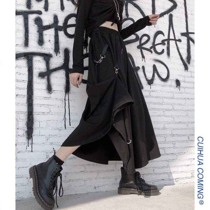 Punk style irregular black skirt with buckles, high waist, paired with combat boots against graffiti wall.