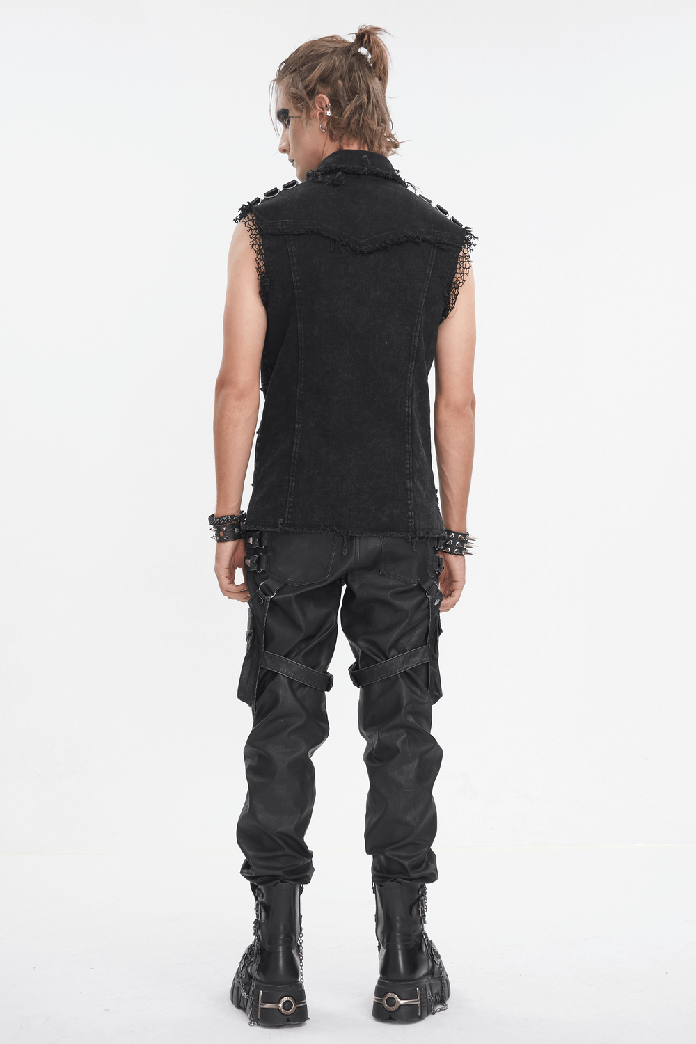 Back view of a man wearing a punk style sleeveless black studded vest with gothic pants and boots.
