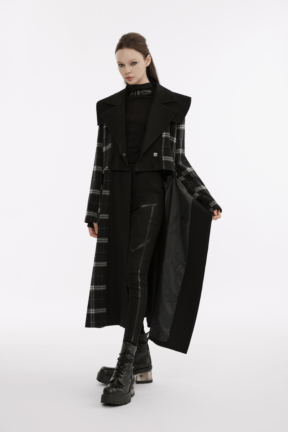 Model showcasing punk techwear in long plaid coat over black outfit with edgy faux leather leggings and combat boots.