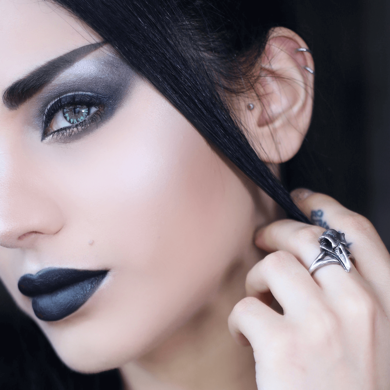Close-up of a person showcasing a raven skull ring in antiqued pewter with bold gothic makeup and dark lips.