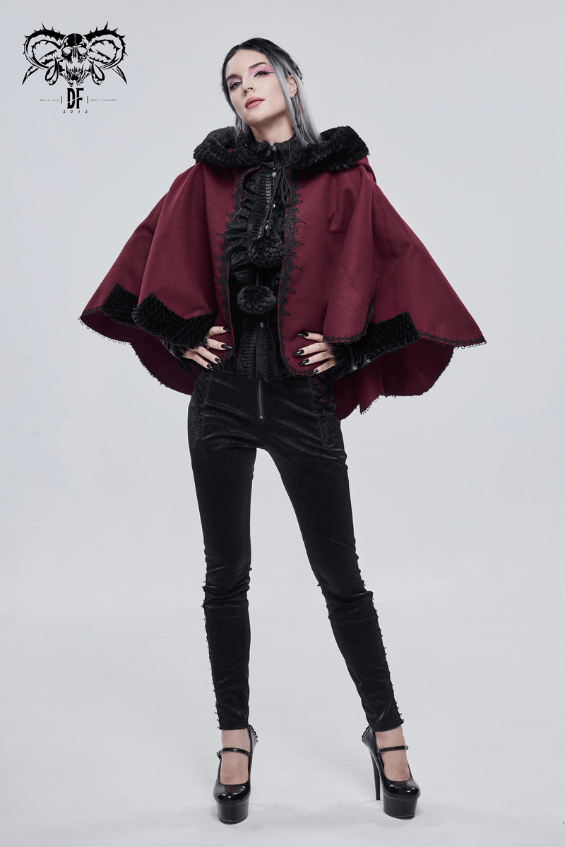 Model wearing a red gothic short hooded cloak with black fur and pompons, stylishly posing in a black outfit.