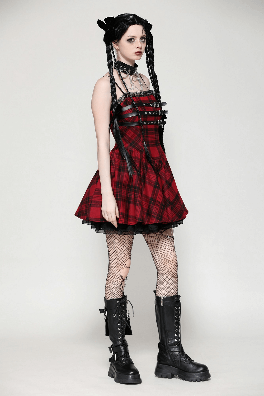 Red plaid Gothic mini dress with lace-up back and buckle details, paired with fishnet stockings and combat boots.