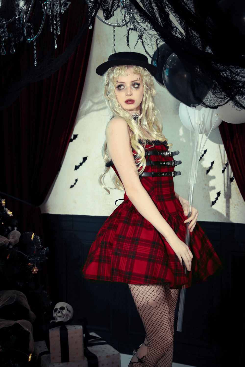 Punk-inspired red plaid Gothic mini dress with buckle details, styled with a black hat and balloons against a spooky backdrop.