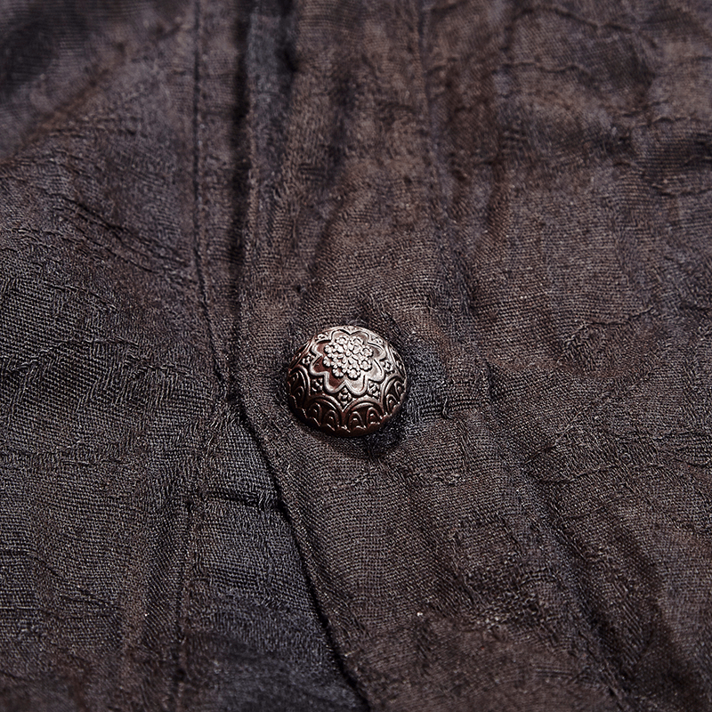 Close-up of an intricately detailed vintage button on a textured black linen fabric.
