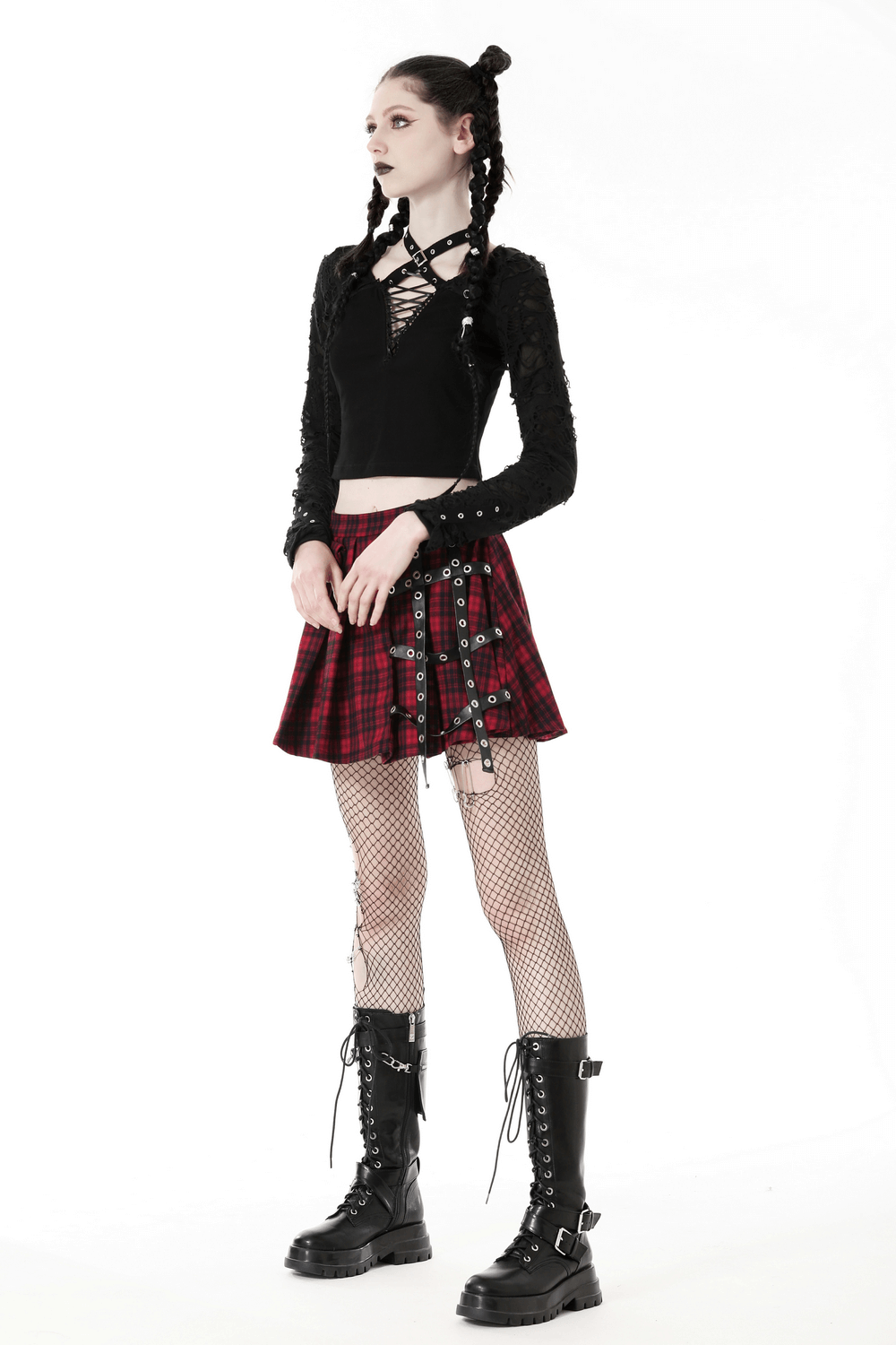 Edgy model in ripped long sleeve crop top and plaid skirt, showcasing a rockstar style with lace-up details and combat boots.