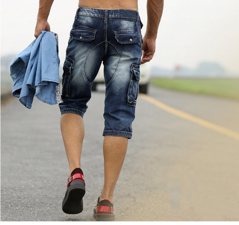 Man wearing rock style cargo shorts and holding a denim shirt, walking on a road, showcasing casual summer fashion.