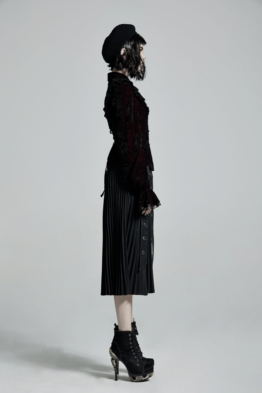 Gothic women's outfit featuring a ruffled velvet blouse and pleated black skirt, styled for dark elegance.