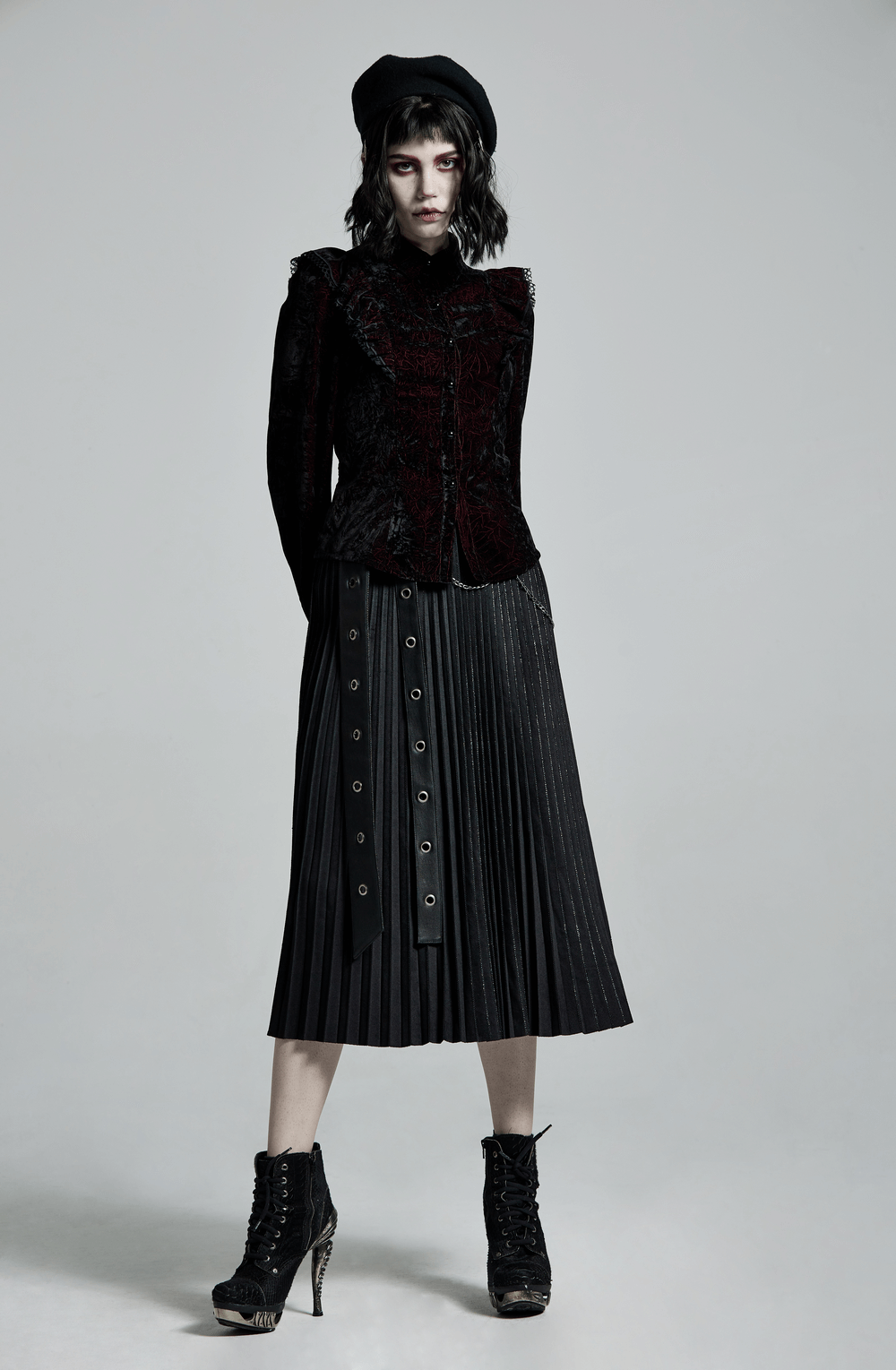 Model wearing a ruffled velvet gothic blouse with lace-up back, paired with a pleated skirt and stylish heels.