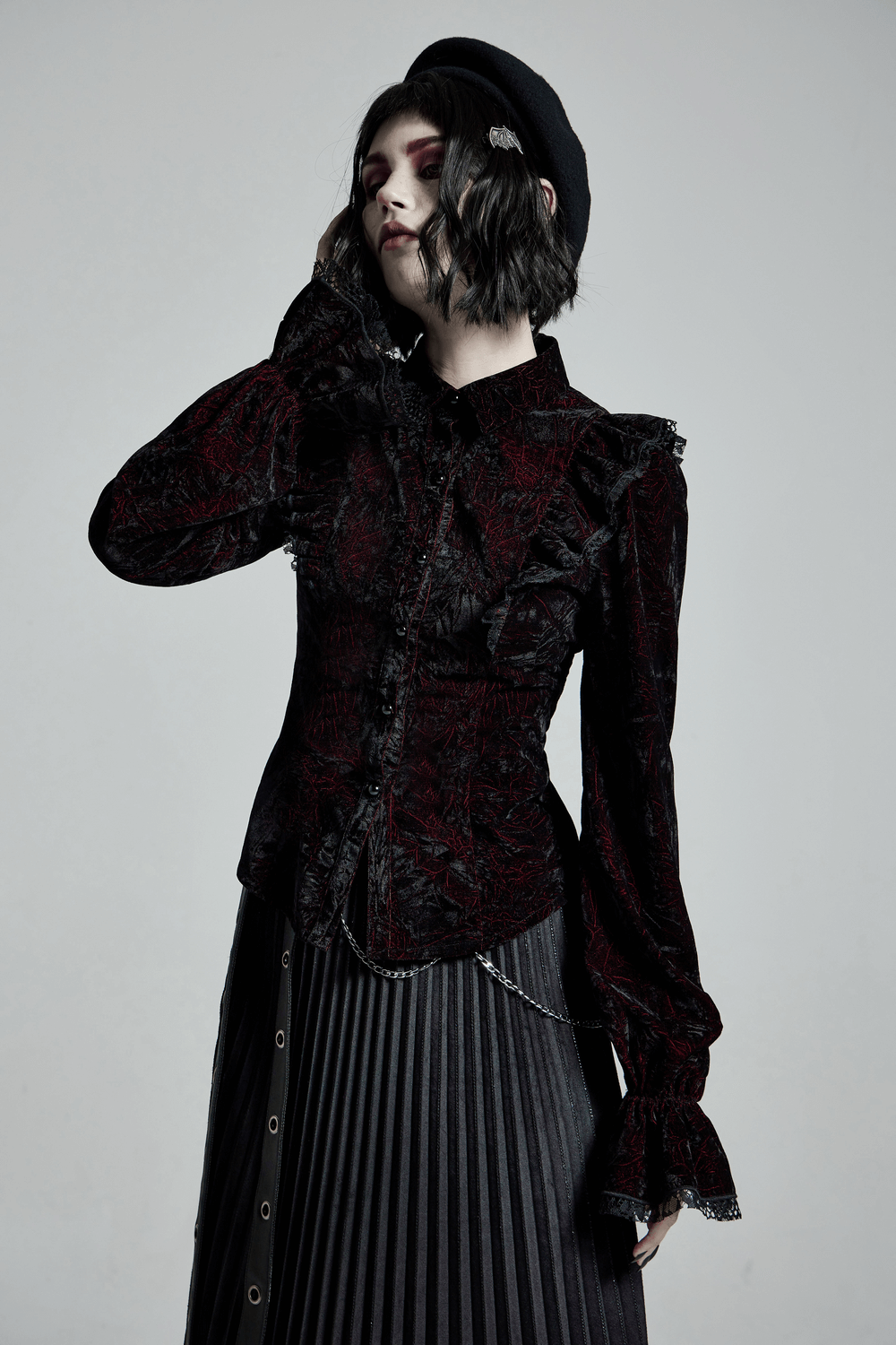 Gothic women's ruffled velvet blouse with lace-up back, styled elegantly with a pleated skirt.