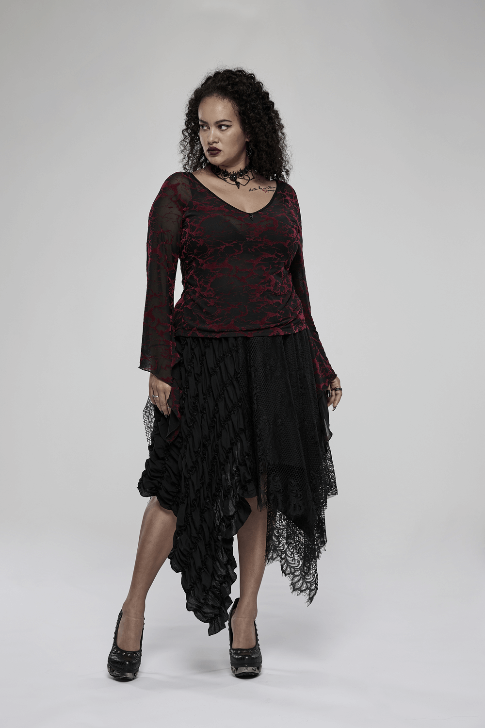 Woman in scarlet abstract V-neck mesh goth top paired with a flowing black asymmetrical skirt.