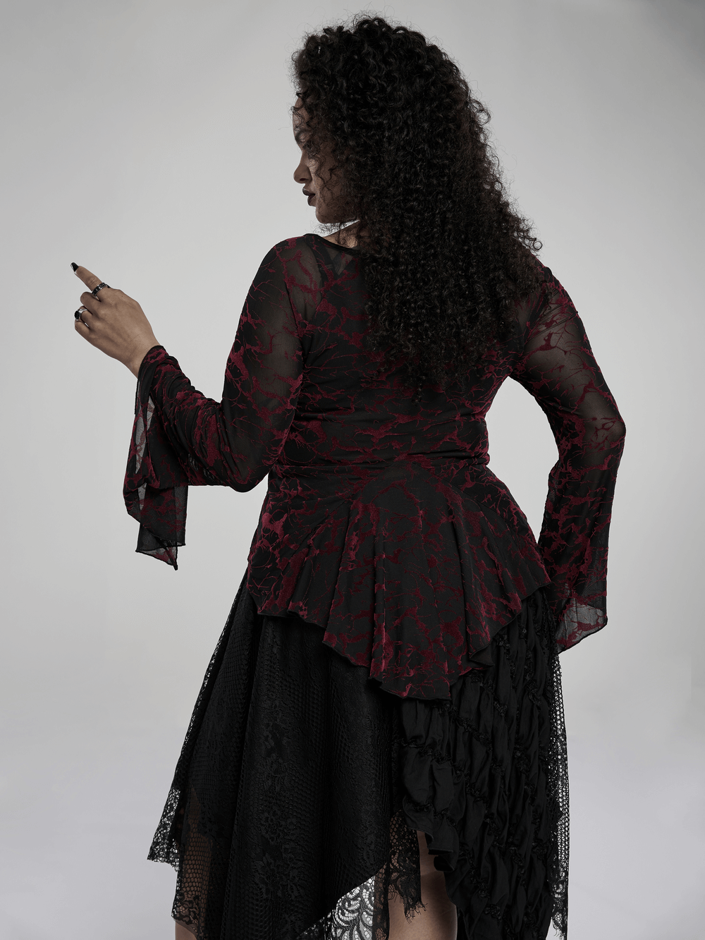 Back view of a woman in a scarlet abstract V-neck mesh top, showcasing elegant flared cuffs and gothic style.