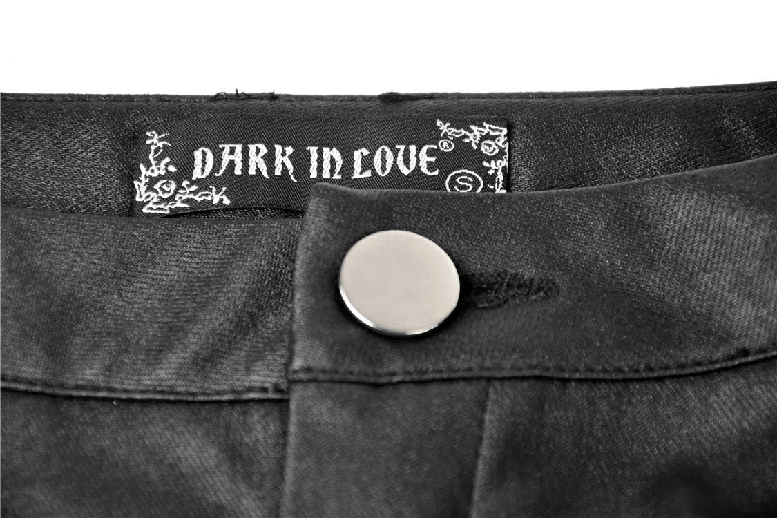 Close-up of the DARK IN LOVE label on black skinny pants showcasing metal button detail.