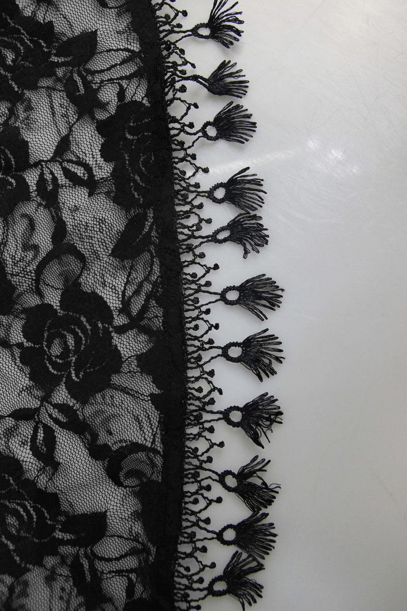 Close-up of black lace fabric with floral patterns and ornate fringed trim.