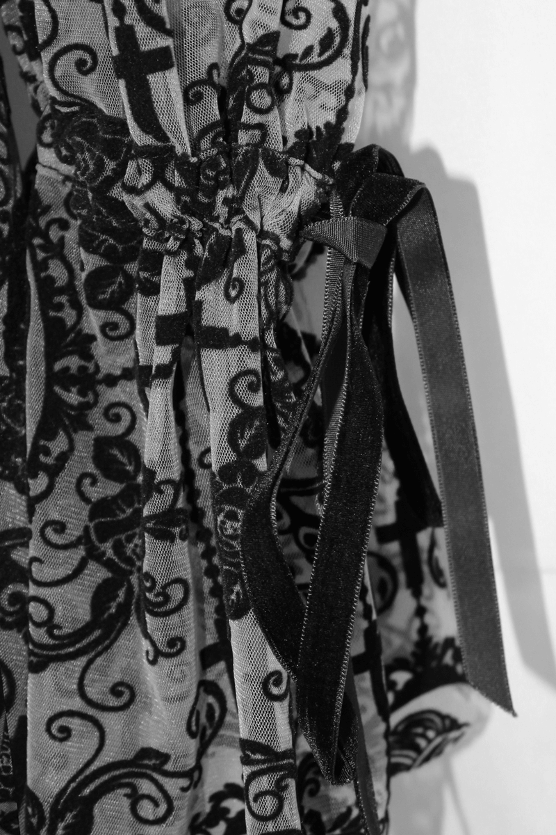 Detail of sexy black lace dress with elegant ribbon ties and gothic cross patterns.