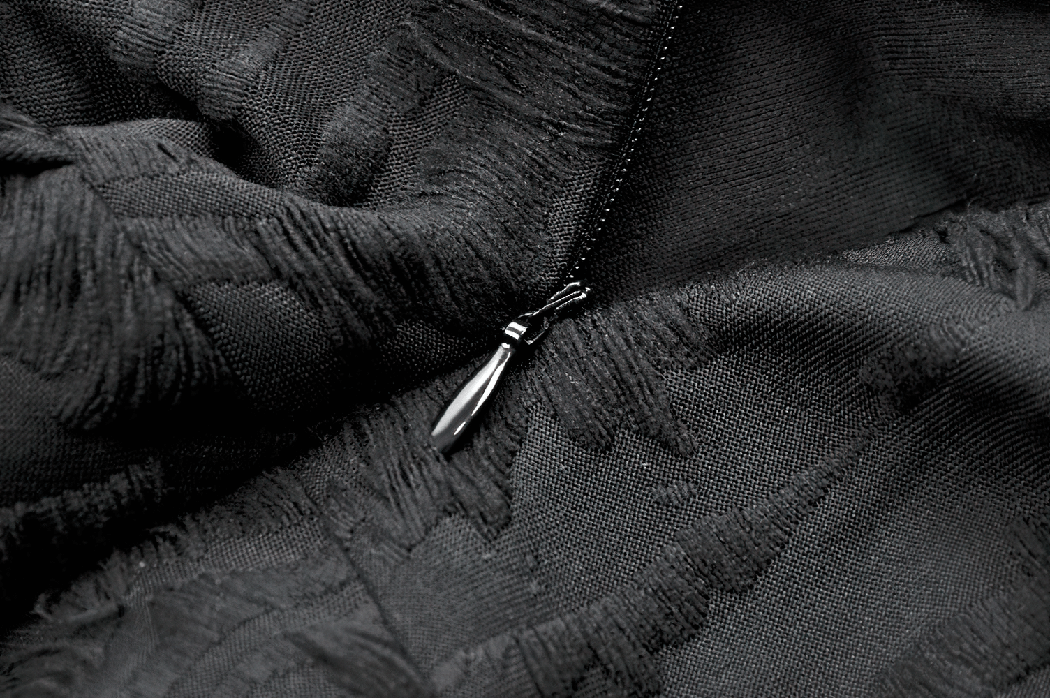 Close-up of a black zipper on textured fabric, showcasing elegant detailing perfect for a stylish dress.