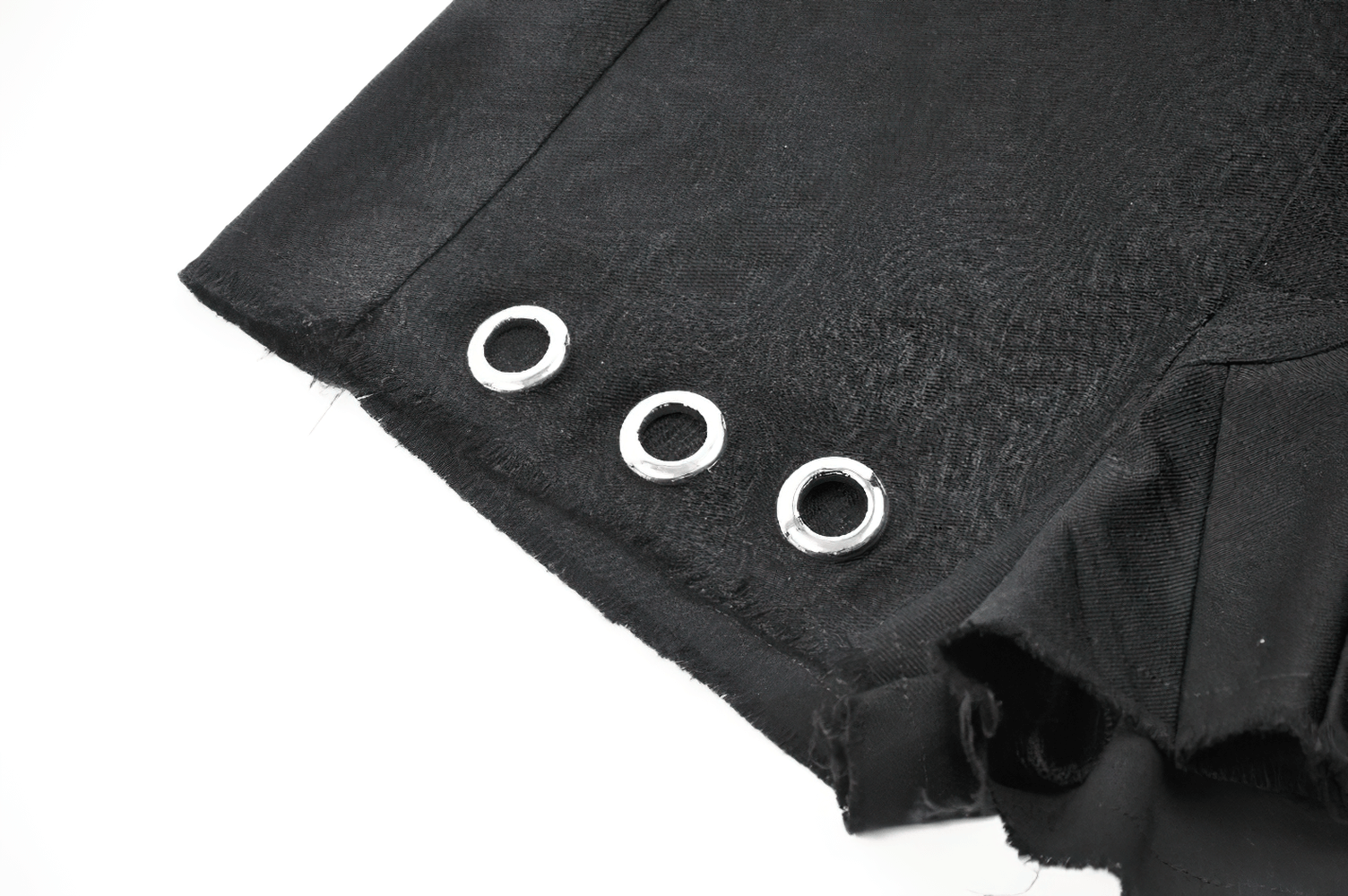 Close-up of black pleated shorts featuring silver eyelet details and a raw hem finish.