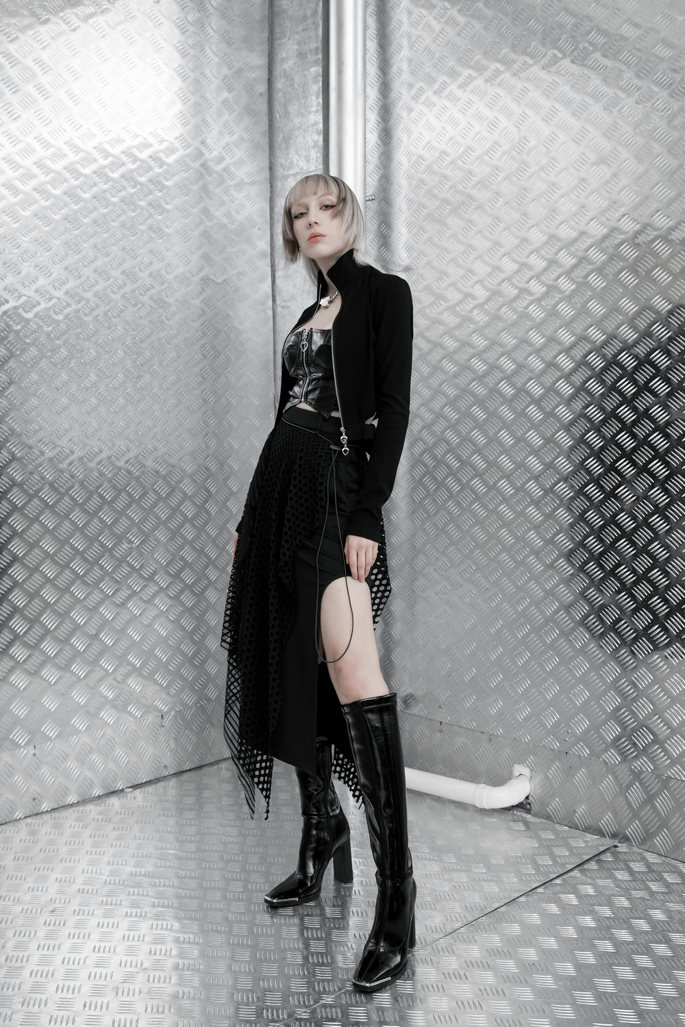 Model in a sexy punk rave outfit featuring a black zipper crop camisole and stylish black skirt on a metallic background.