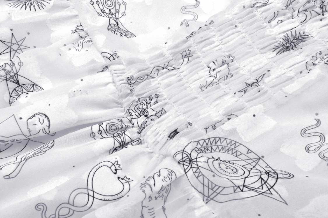 Close-up of a white fabric featuring mystical black illustrations on a punk strap dress.