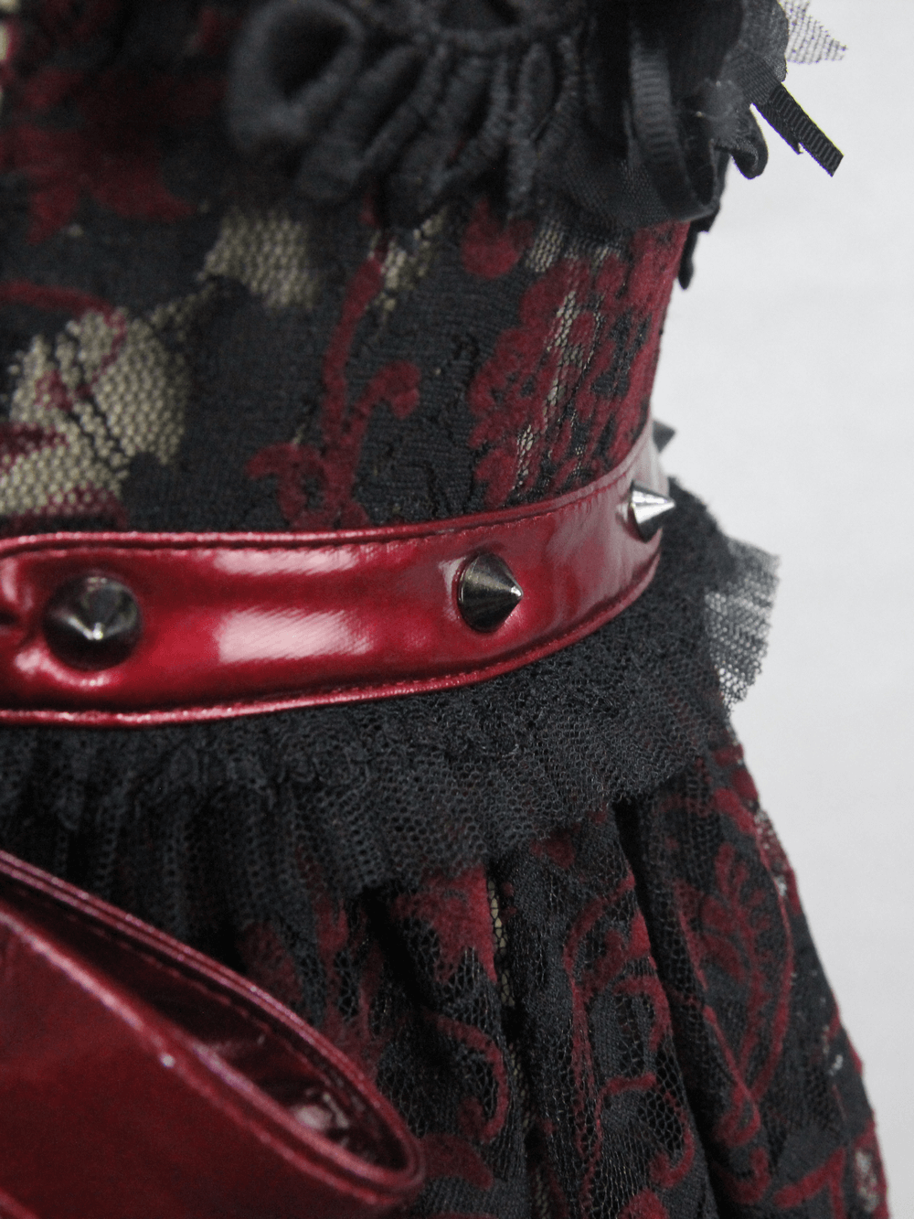 Close-up of a black lace dress with burgundy accents, featuring spiked belt and detailed lace trim for a gothic look.