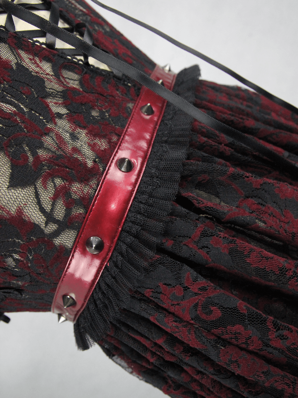 Close-up of black lace gothic dress with red detailing and lacing, showcasing intricate lace patterns and edgy design.
