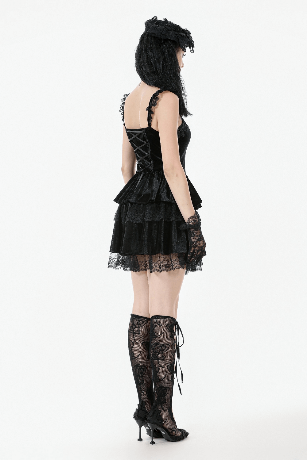 Gothic black velvet tiered mini dress with lace trim and corset design, worn with lace stockings and heels.