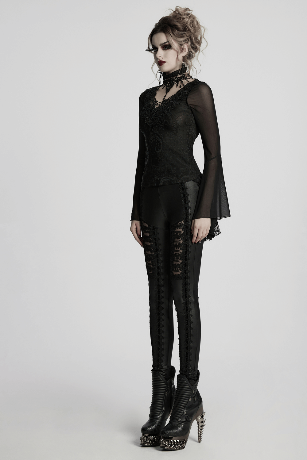 Gothic model wearing a sheer lace top with bell sleeves and choker, paired with edgy black pants and boots.
