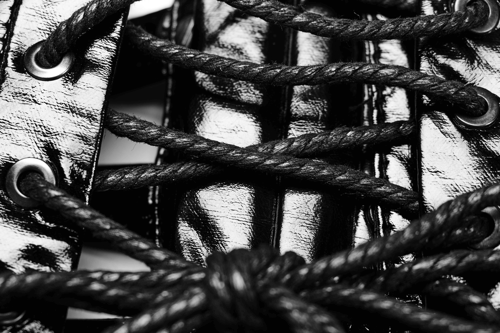 Close-up of shiny black patent corset lacing with thick ropes and eyelets, showcasing punk style details.