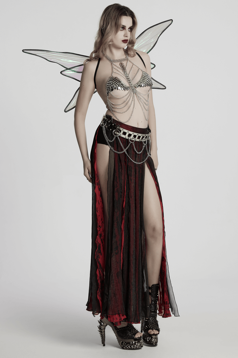 Model in silver dragon scale chain bra harness and black skirt with red accents and wings for a bold festival look.