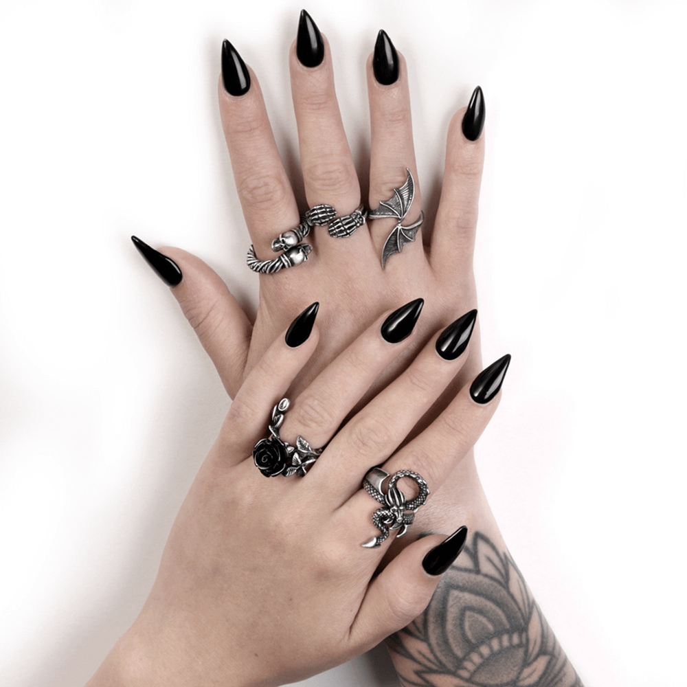 Stylish black nails adorned with gothic rings featuring skeletons, roses, and intricate designs for a striking look.