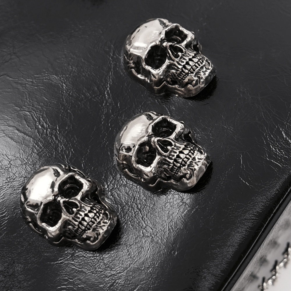 Close-up of silver skull charms on a black faux leather tote bag, showcasing gothic style and edgy detail.