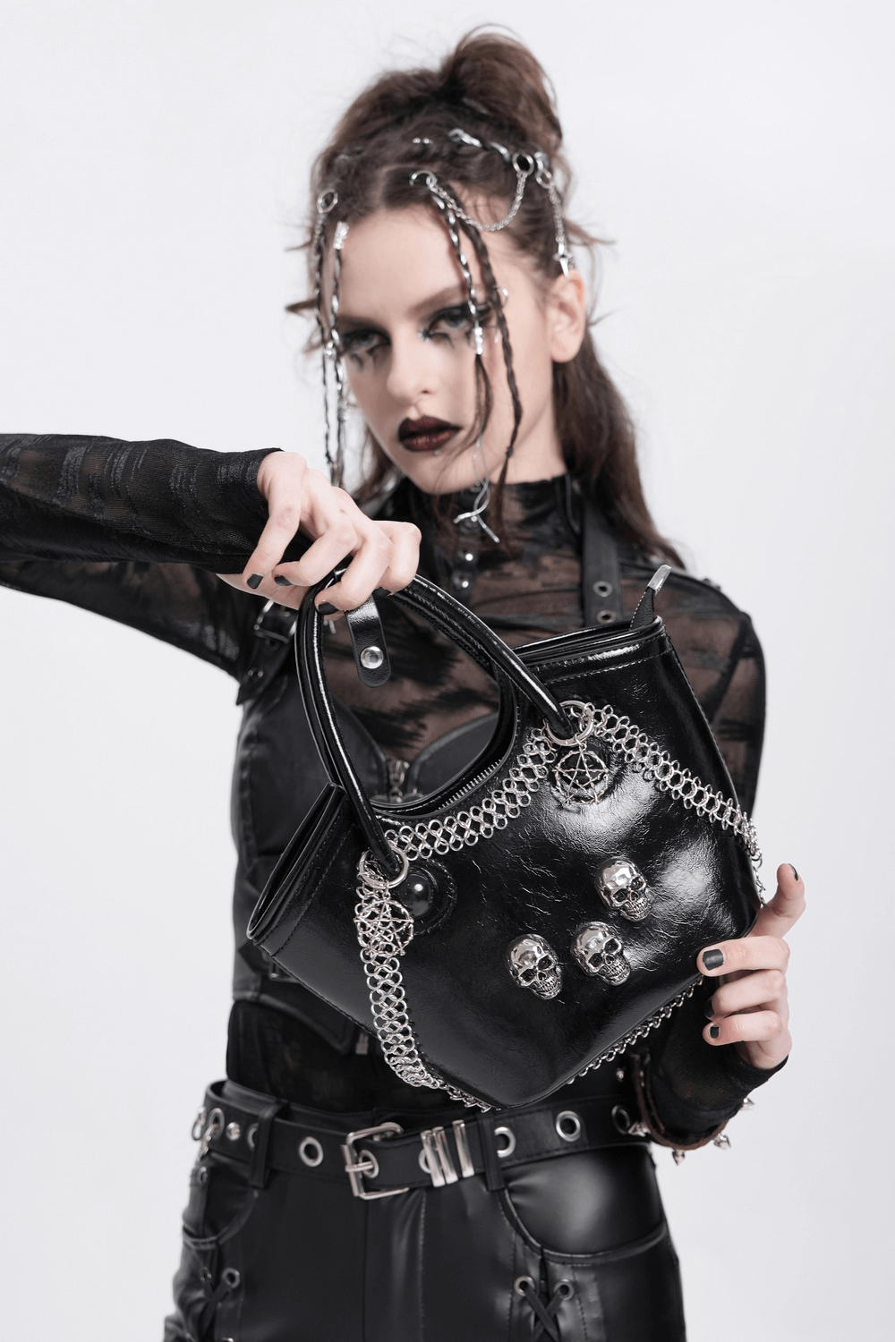 Gothic black tote bag with skull details and chain accent held by a model in edgy attire.