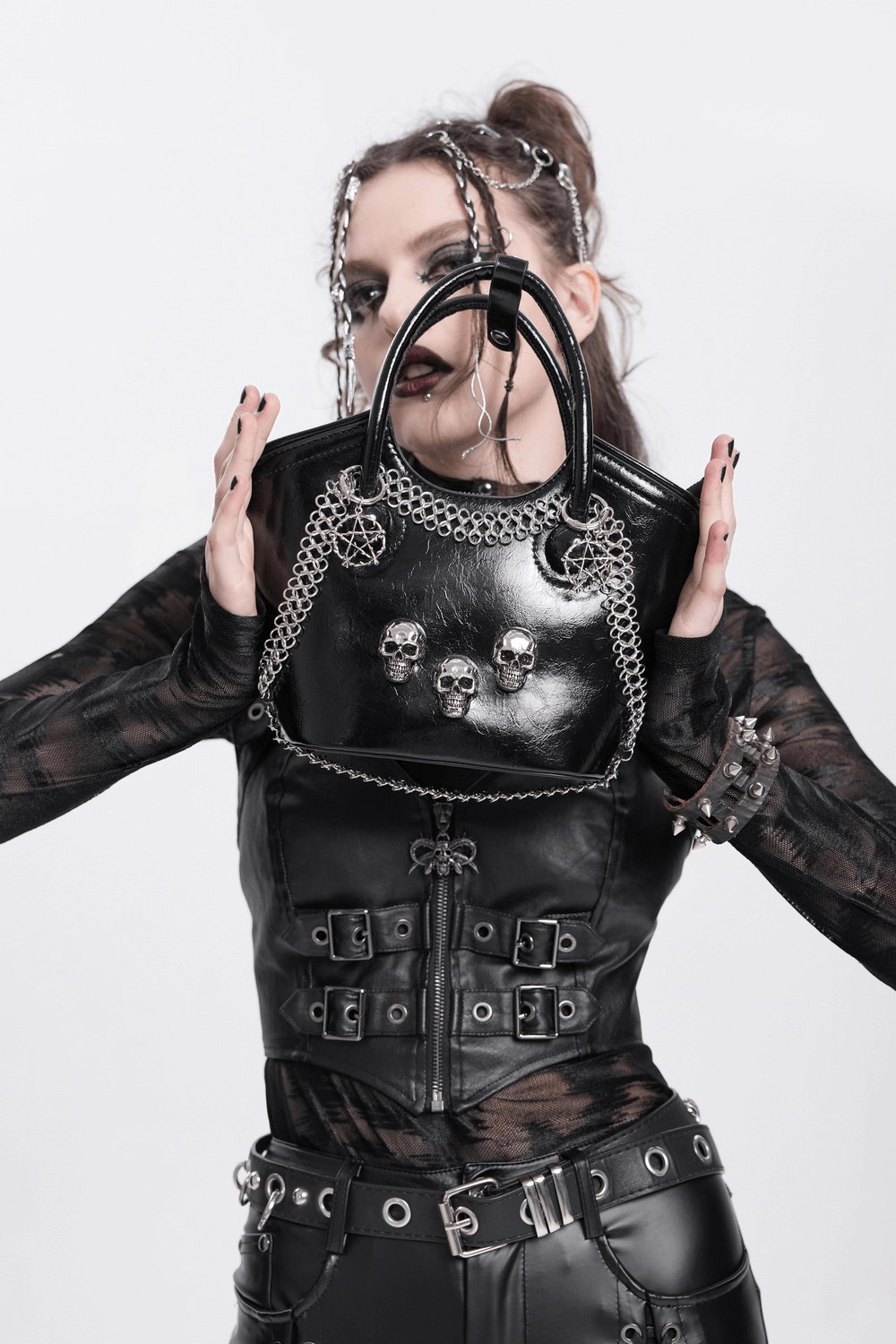 Edgy gothic tote bag with skull accents and chain detail, held by a model in stylish black leather outfit.