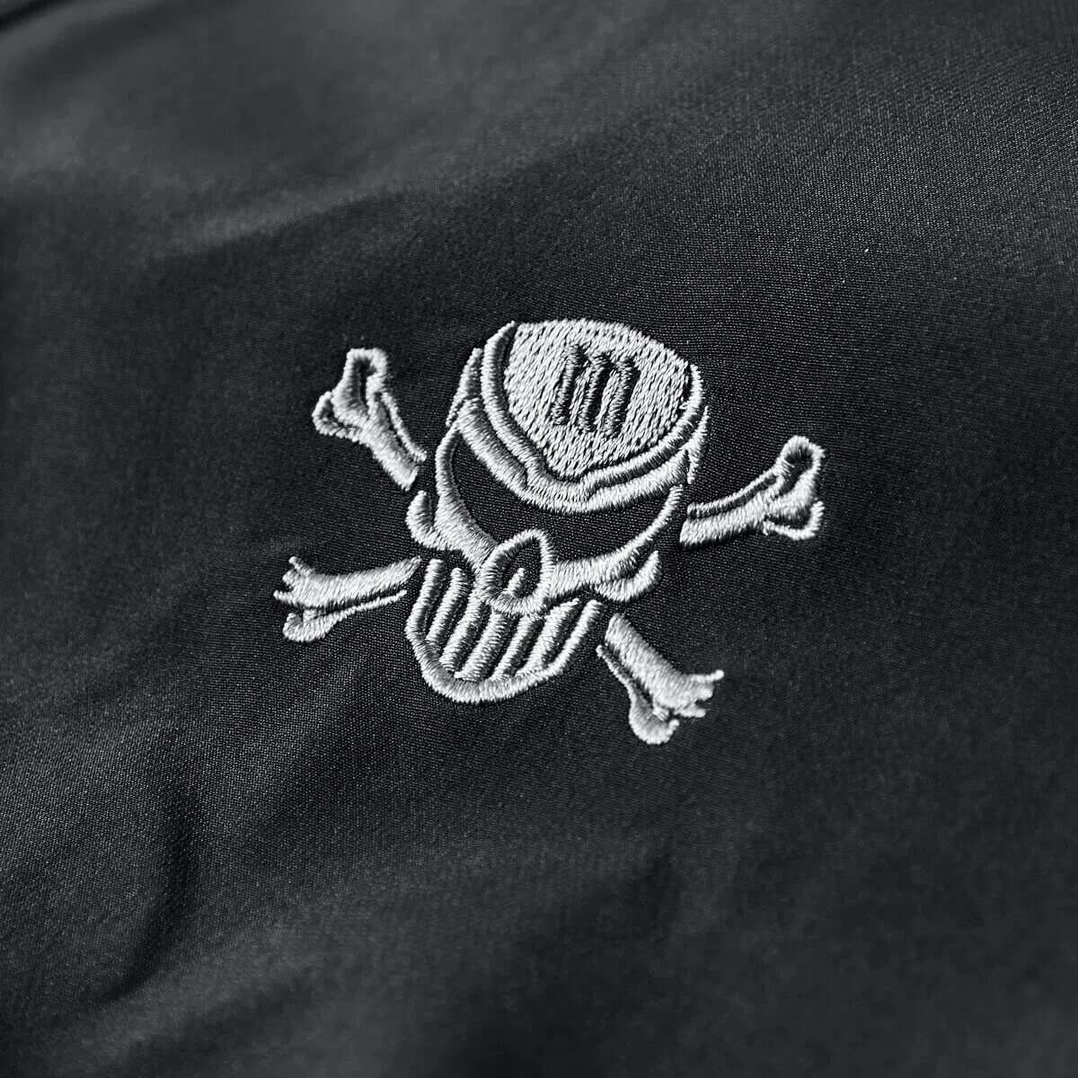 Skull and crossbones embroidery on a sleek black bomber jacket, showcasing edgy military-inspired design.