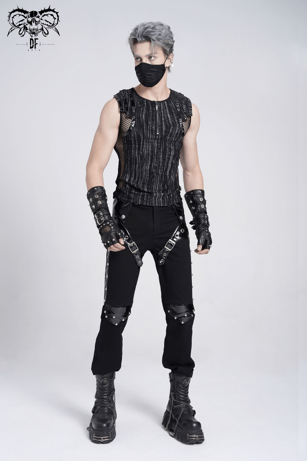 Model in sleeveless gothic top with mesh, black pants, and buckles, showcasing punk grunge style.