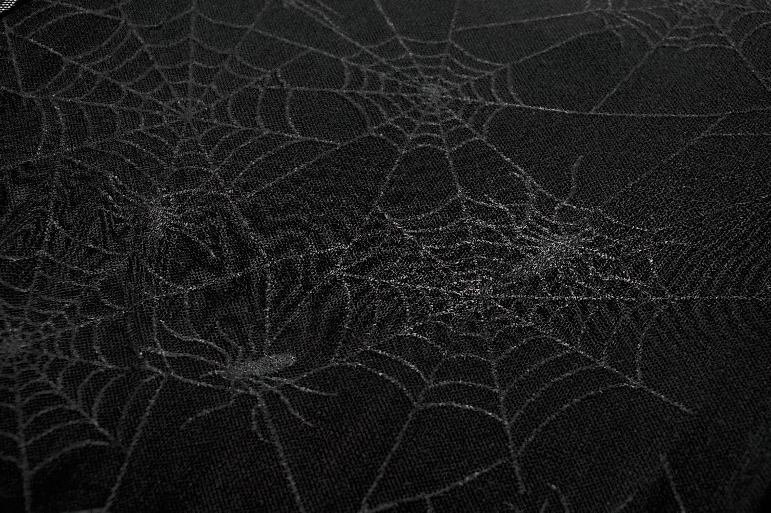 Close-up of a spiderweb pattern on black fabric for a stylish lace-up dress design.