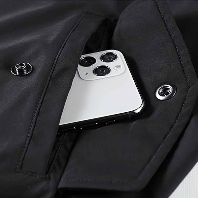 Close-up of a smartphone tucked inside the pocket of a sleek black bomber jacket.
