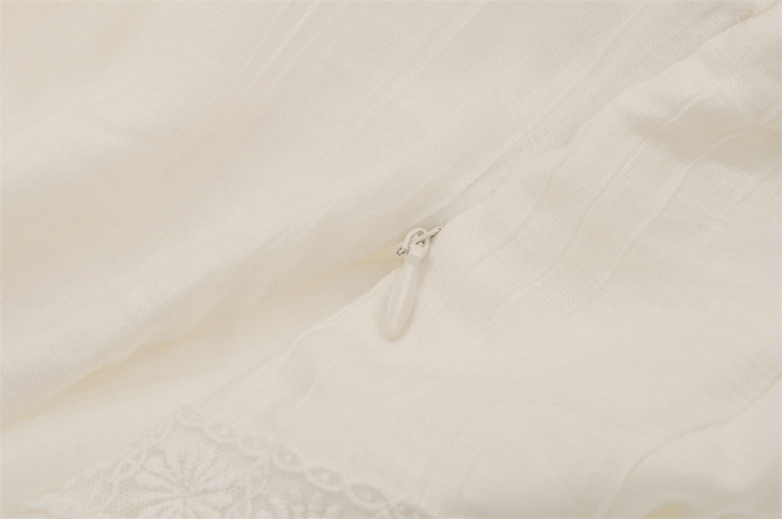 Close-up of romantic white lace blouse fabric with delicate detailing and zipper.