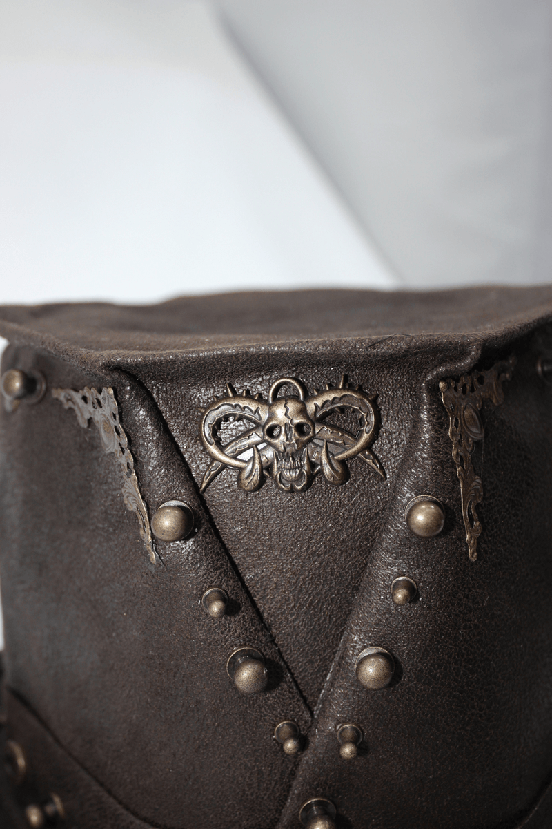 Close-up of a steampunk brown PU leather hat with metal rivets and skull decoration.