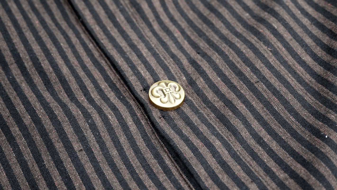 Close-up of the vintage steampunk striped shirt showing a stylish brass button detail.