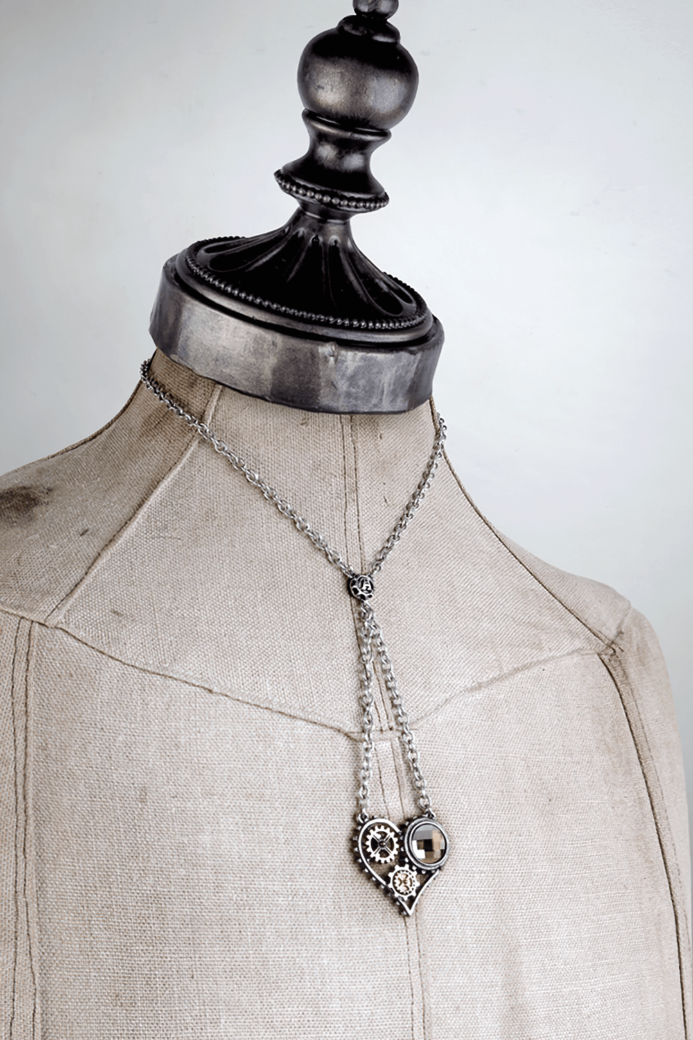 Steampunk Heart Pendant with Gears and Crystal Accent displayed on a vintage mannequin, showcasing its industrial elegance.