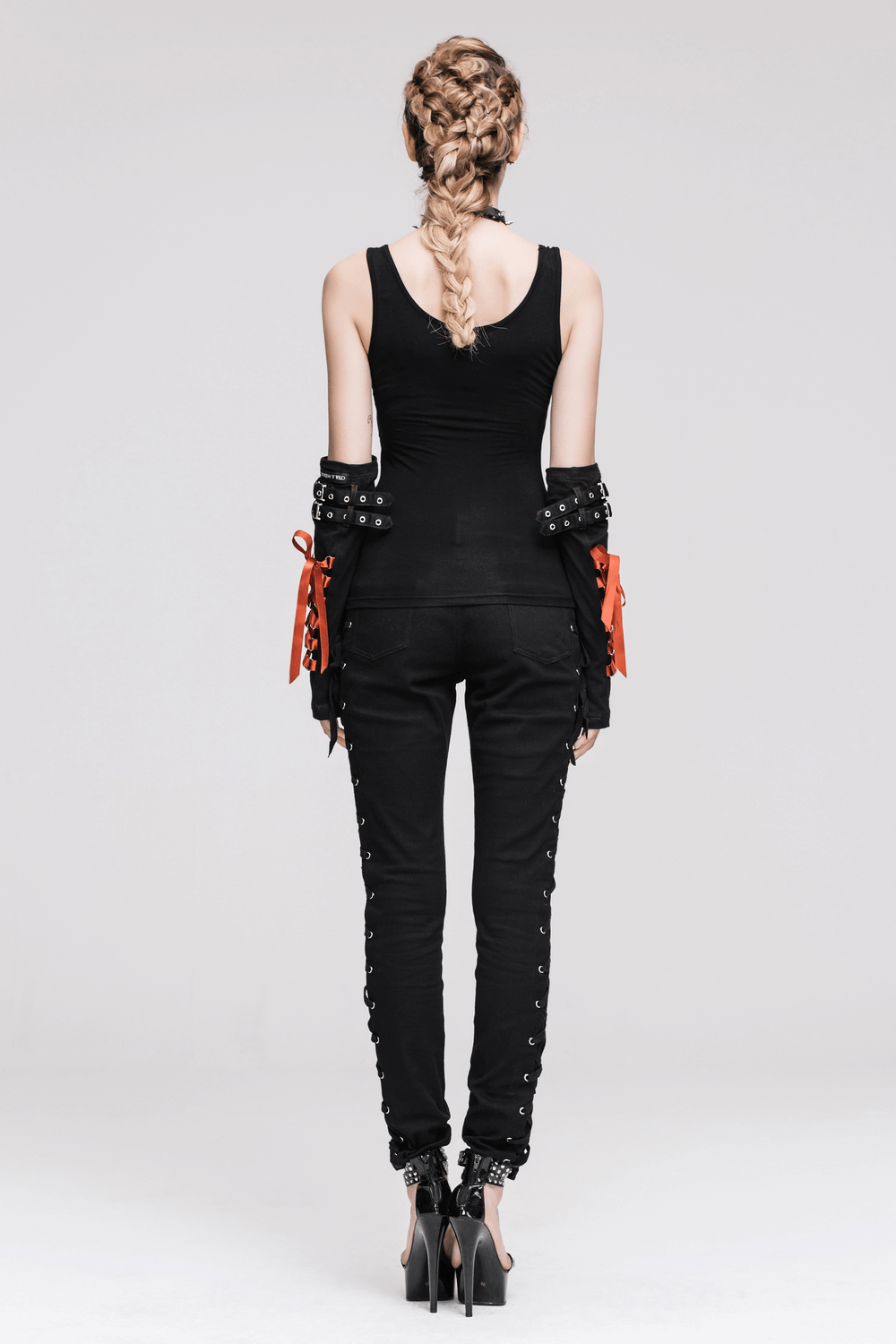 Back view of a woman in a steampunk black tank top with spikes and stylish black pants, showcasing edgy fashion.