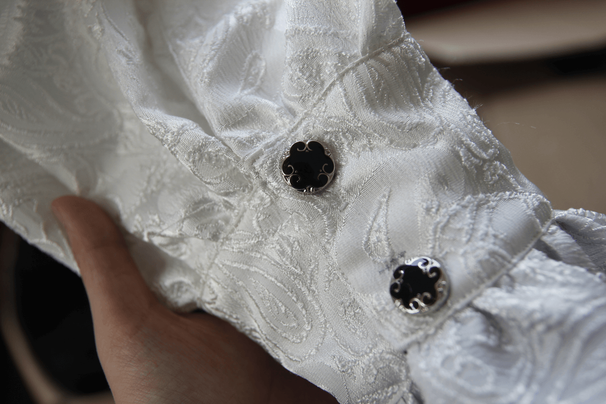 Close-up of a steampunk white men's shirt sleeve showcasing ornate black buttons and intricate fabric pattern.