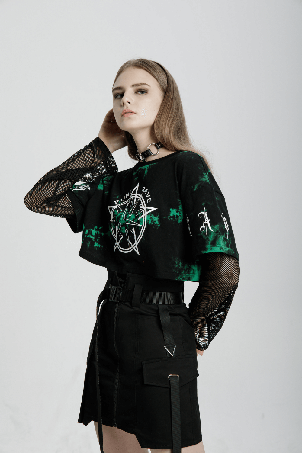Edgy model wearing a cropped black mesh shirt and asymmetric high-waisted tactical skirt, embracing urban punk style.