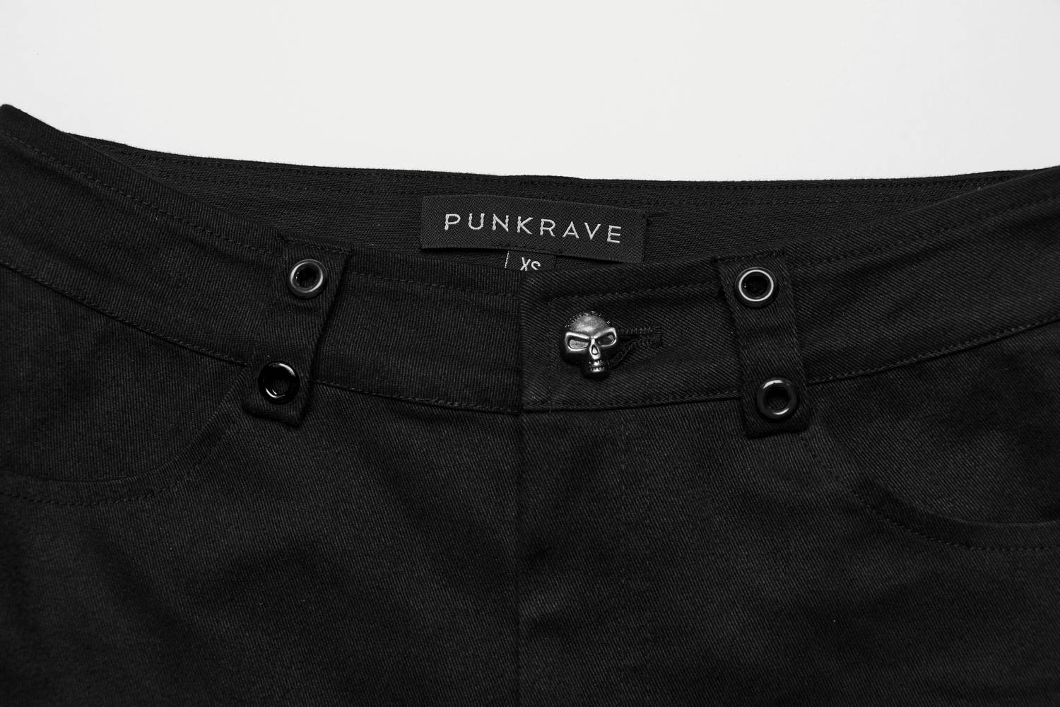 Close-up of black gothic flared pants featuring a skull accent button and PUNK RAVE label.