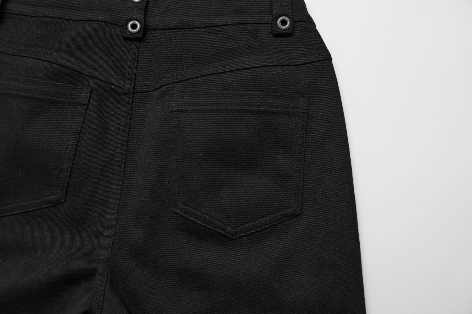 Back view of black stretch gothic flared pants showcasing pocket details and skull accent buttons.