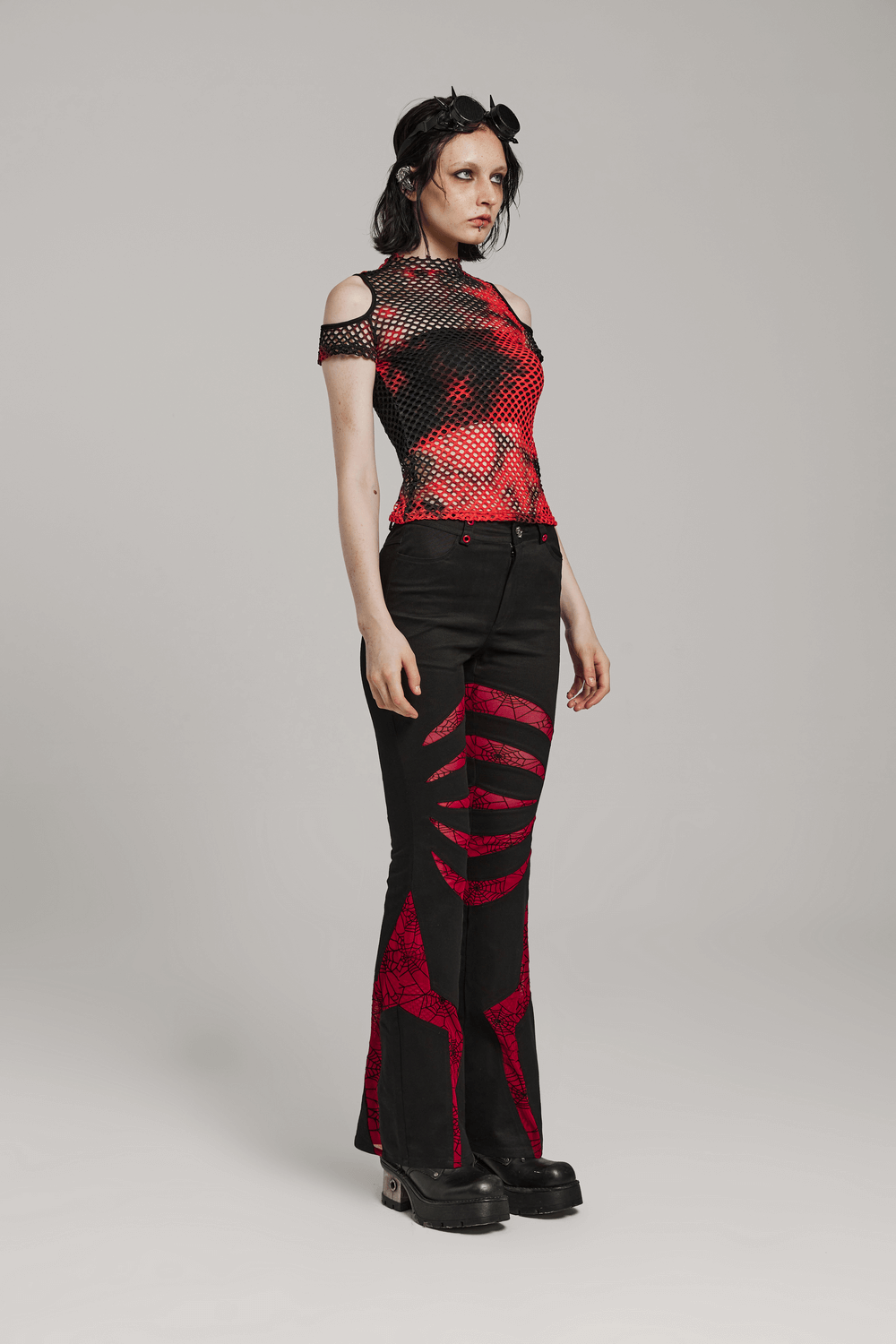 Goth style model in black and red spiderweb flared pants with matching mesh top, perfect for edgy fashion.
