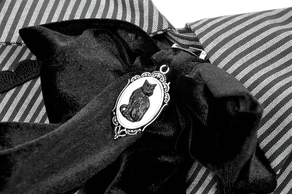 Close-up of a black cat pendant on a striped blouse with a dramatic bow detail and lace elements.