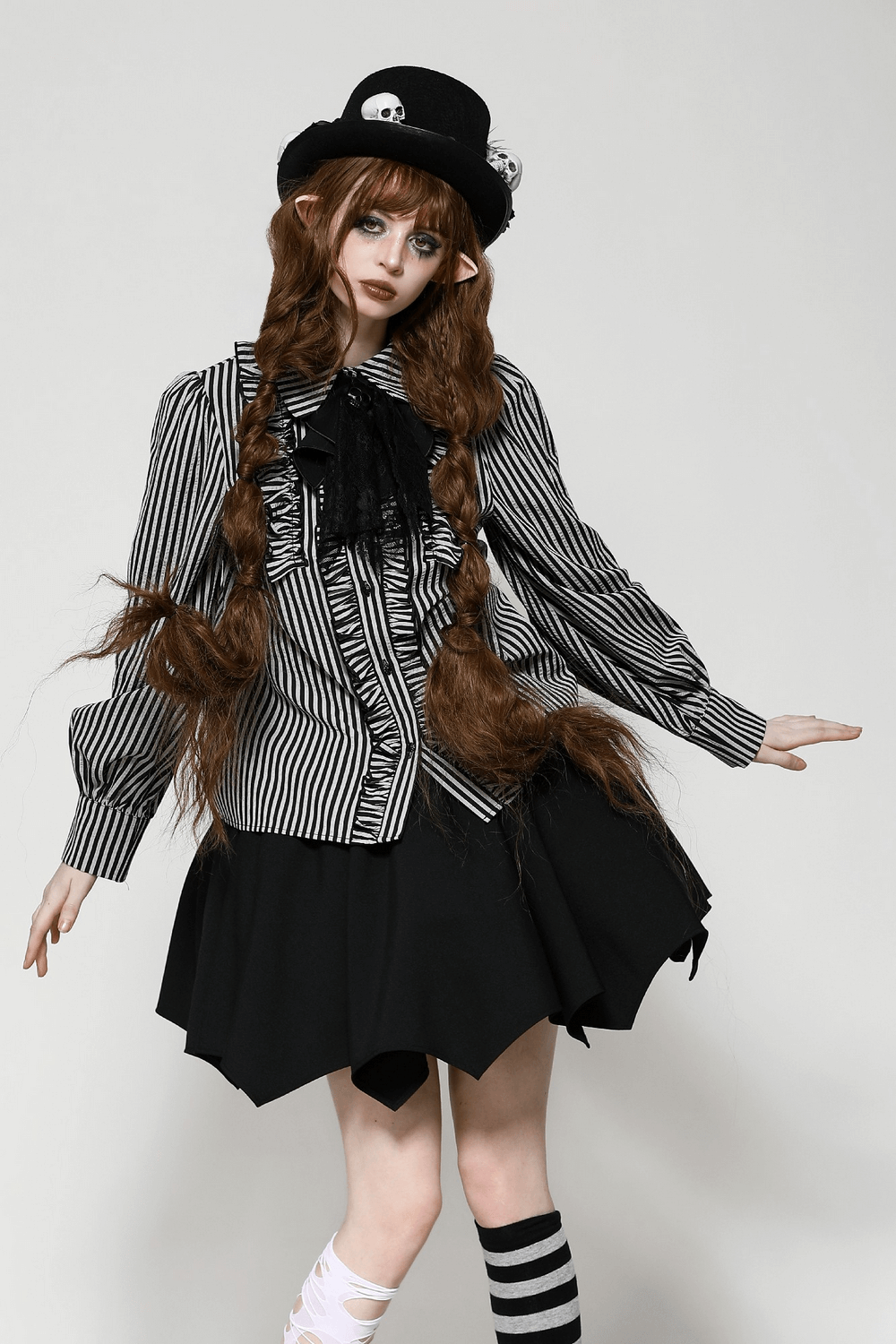 Striped gothic blouse with lace details, ruffles, and skull accent, paired with a black skirt and whimsical hat.